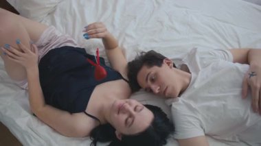 Genç bir adam ve kadın yatakta uzanmış kalp şeklindeki oyuncaklarla övünüyorlar. Yatak odasında sevgililer gününde poz veren beyaz bir çift.