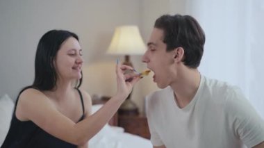 Yandan bakıldığında, gülümseyen genç bir adam bir kadınla sevgili gibi konuşuyor erkek arkadaşını lezzetli bir tatlıyla besliyor. Kafkasyalı çiftin mutlu bir sabah geçirmesini dilerim.