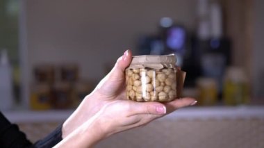 Beyaz kadın ellerinde fındık olan yakın çekim kavanozu. Tanımlanamayan genç bir kadın lezzetli besleyici fındıkları kapalı mekanda tanıtıyor.