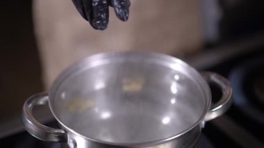 Eldivenle kaynar suya yavaş yavaş tuz serpiyorsun. Lokanta mutfağında yemek pişirmek için tanınmayan kadın tuzlama sıvısı pişiriyor.
