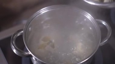 Yakın çekim yüksek açı görüntüsü kaynayan suya çiğ hamur tatlısı karıştırıcı yemeği kaşıkla ekliyor. Tanımlanamayan bir kadın restoran mutfağında lezzetli yemekler pişiriyor.