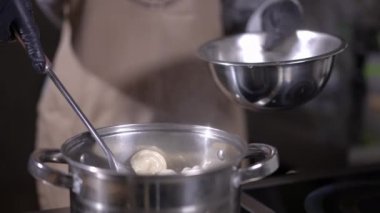 Tanınmayan aşçı, tencerede kaynar su bulunan tencereden pişirilmiş hamur köftelerini çıkarıyor. Eldivenli bir kadın restoranın mutfağında lezzetli bir akşam yemeği hazırlıyor.