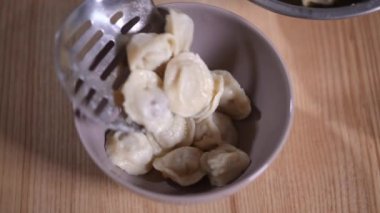 Mantı ile yakın çekim kasesi ve içine lezzetli yiyecekler koyan yağsız ellerle. Yakından tanınmayan aşçı yavaş çekimde kafe mutfağında lezzetli bir yemek siparişi hazırlıyor.