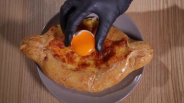 Geleneksel Gürcistan khachapuri 'sine yumurta sarısını yavaşça yerleştiriyorum. Kadın eldiveni. Lezzetli yemek artıklarına malzeme ekliyor.