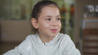 Ön manzara, kafeteryada oturup yemek yiyen neşeli beyaz bir kız. Neşeli mutlu çocuğun portresi ağır çekimde lezzetli yemekler yiyor.