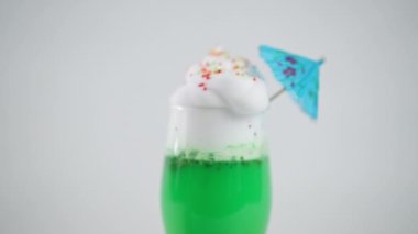 Kapalı yeşil kokteyl ve krem şanti karışımı. Yakın plan lezzetli, beyaz arka planda mavi şemsiyeli smoothie.