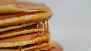 Solda altın bal damlalarının yavaş çekimde aktığı krep yığını var. Beyaz arka planda lezzetli bir brunch tatlısı.