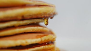 Yavaş çekimde krep yığınının kenarına düşen bal damlaları. Aşırı yakın çekim solda beyaz arka planda lezzetli tatlı