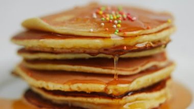 Çok renkli şeker toplarının bal şurubunun üzerine döküldüğü yakın plan krep yığını. Kapalı, lezzetli, kahvaltı için lezzetli yiyecekler.