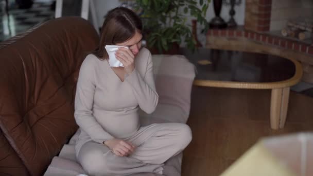 広いショット欲求不満妊娠中の若い女性がリビングルームでソファに座って泣いています 紙組織で涙を拭く悲しい表情で落ち込んだ白人の肖像 — ストック動画