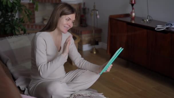 宽镜头迷人的正怀孕妇女挥动说话使用视频聊天在数字平板电脑上 快乐自信的白种人年轻人在网上聊天 坐在客厅的沙发上 — 图库视频影像