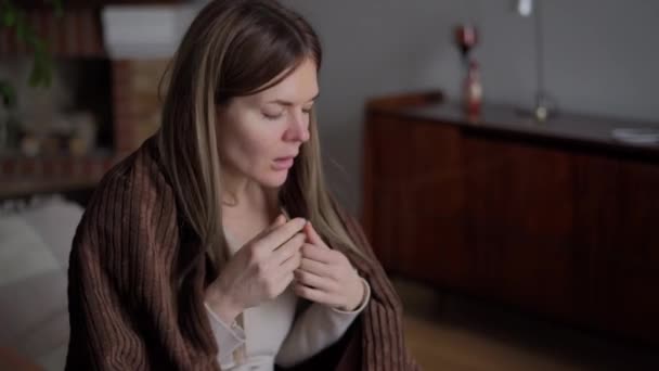 体温計で体温を測定熱を持つ若い咳の女性の肖像画 病気コーカサス人女性摩擦腕座っています上のソファラップで毛布 — ストック動画