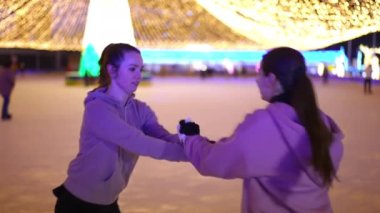 Buz pistinde el ele tutuşarak ağır çekimde dönen iki yetenekli sporcu kadın. Beyaz tenli, buz pateni giymiş zarif kadınlar Noel arifesinde dışarıda eğitim görüyorlar.