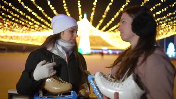 在平安夜的溜冰场中 两名自信的年轻女子与冰鞋站在一起聊天 积极的白人女运动员在户外活动后聊天 — 图库视频影像