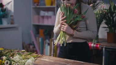 Lale kokan, masa üstüne çiçek koyan buket yapan genç bir kadın. Beyaz kadın çiçekçi. Kapalı alanda çiçekçide çalışıyor.