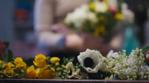 バックグラウンドで花束を作るぼやけた若い花のクローズアップ黄色と白の花 フラワーショップで働く未知の白人女性 デザインを構成する — ストック動画
