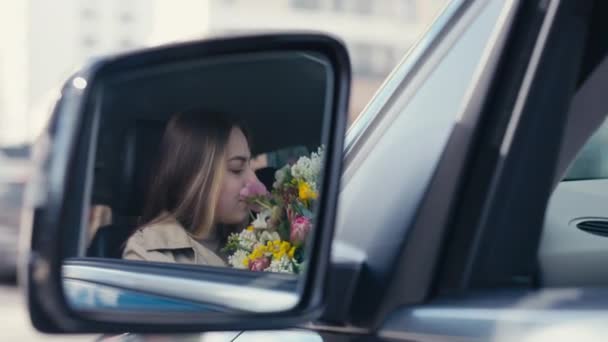 笑容满面的年轻女子嗅着花束向远方望去的车的侧视镜中的倒影 心满意足的白种人女士 满载鲜花 — 图库视频影像