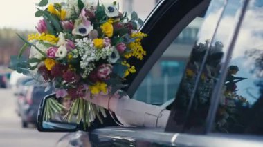 Sürücülerin penceresinden dışarı süzülen kadın eli yolda. Şehir merkezinde arabasında çiçekleri olan tanınmayan beyaz bir kadın.