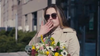 Açık havada güneşin altında duran güzel, pozitif ve güzel bir genç kadının portresi. Mutlu, kendine güvenen, çiçekli beyaz kadın şehir şehrinde güneşli bir gün geçiriyor.