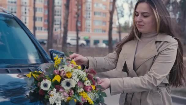 笑顔の若い女性は 都市の通りで車のフードに花束を見つけます 幸せな満足した白人女性の肖像画とバレンタインサプライズ花屋外 — ストック動画