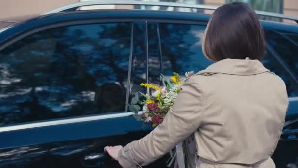 现场摄像头跟随年轻女子走向汽车 坐在司机座位上 开着花束门 自信的白种人优雅的女士 户外开着花 — 图库视频影像