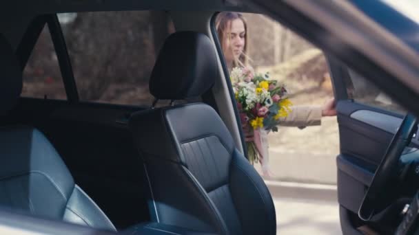 白人年轻女子走向汽车 坐在司机座位上闻着花香 城市里开着汽车的快乐而自信的女士 — 图库视频影像