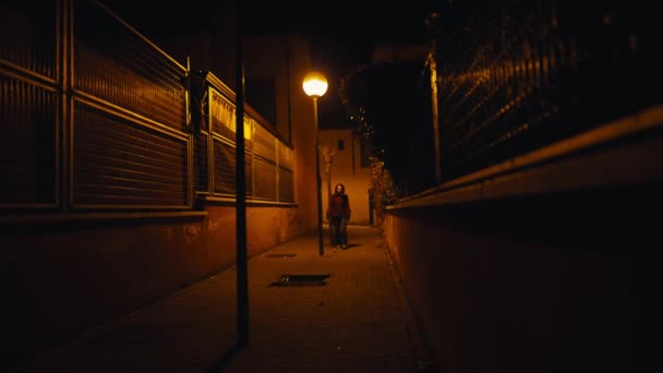 暗闇の中の狭い街路で 白人女性が背景から歩いて出て行く ワイドショット自信あふれる女性が街の外で夜を散策 — ストック動画