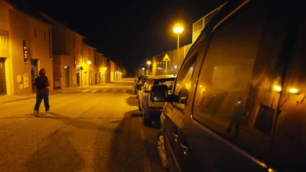 成排的汽车在夜晚停在城市街道上 妇女从左边经过 难以辨认的白人女士在黑暗中漫步 户外点着黄色路灯 — 图库视频影像