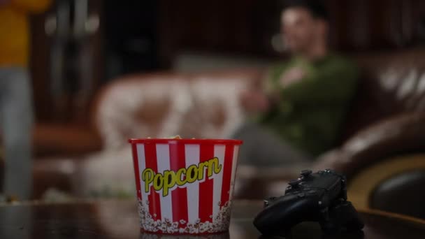 Närbild Spelkontroll Och Popcorn Bordet Med Suddiga Män Sitter Ner — Stockvideo