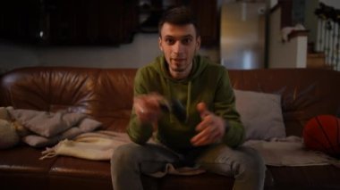 İçine kapanık yetişkin oyuncu portresi karanlıkta kanepede oturmuş joystick ile oyun oynuyor. Ön görüş odaklı Kafkas genç adam evde online oyun oynuyor.