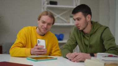 Akıllı telefon uygulamasında sosyal medyada konuşan iki genç adam masada oturuyor. Dertsiz tasasız Kafkasyalı dostların evde dedikodu yaptığı portresi.