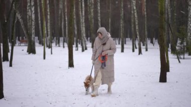 Geniş açıyla gülümseyen, güzel bir kadın. Tasmalı bir köpek yavrusuyla karda yürüyor. Kış ormanında köpekle gezen Kafkas 'lı güzel bayan eğlencenin tadını çıkarıyor. Yavaş çekim