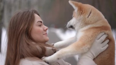 Yandan bakan heyecanlı genç kadın köpek öpen hayvanla konuşuyor gülümsüyor. Kafkasyalı kadın sahibi, hayvanlarla kış sabahının tadını çıkarıyor.