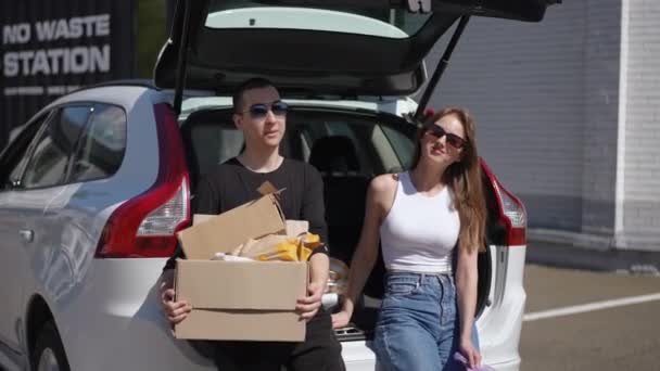 Confident Young Couple Sitting Car Trunk Trash Boxes Looking Camera — Stock Video