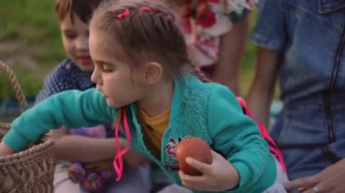 Yoğunlaşmış küçük kız dışarıda piknikte anne ve arkadaşlarıyla oturan elma kokusu alıyor. Odaklanmış büyüleyici beyaz çocuk portresi. Yaz günü boş zamanların tadını çıkarıyor.