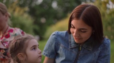 Piknikte çocukla oturan meraklı küçük bir kızla konuşan mutlu beyaz kadın portresi. Gülümseyen büyüleyici anne kızıyla dışarıda eğleniyor.