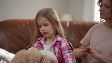 İtaatkar küçük kız oyuncak ayıyla uzun saçlarını tarayan bir kadın gibi oynuyor. Sakin kafkas kızının portresi oyuncak ve sevgi dolu bir anneyle evde çocuğuna bakıyor.