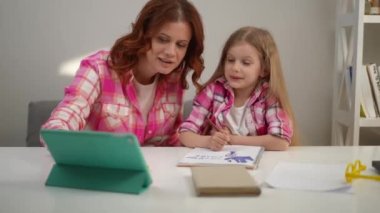 Masada oturup dijital tablette internette sörf yapan pozitif kız ve kadın. Kafkasyalı anne ve kızı evde ödev yaparken konuşuyorlar.