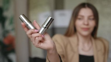 Kapalı alanda kozmetik ürünler gösteren bulanık gülümseyen kadın. Güzellik salonunda makyaj şişeleriyle tanınmayan beyaz bir güzellik uzmanı.