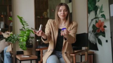 Spa salonundaki sandalyeye oturmuş kozmetik ürünlerle poz veren pozitif özgüvenli güzellik uzmanının portresi. Gülümseyen, ince, beyaz bir kadın. Makyajını övüp duruyor.