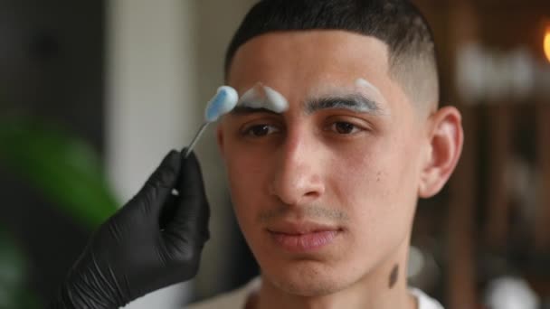 中东年轻人的脸 用女性的手用墨水塑造眉毛 室内美容院自信顾客近照 — 图库视频影像