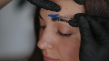 Yakın plan tarama, fırçayla kaplanmış renkli kadın kaşları. Kapalı alanda tanınmayan bir güzellik uzmanıyla genç beyaz bir kadının yakın plan fotoğrafı.