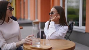 Genç kadınlar kahve fincanlarını getiren tanınmayan bir garson gibi gülümsüyor. İki pozitif Kafkasyalı bayan arkadaş şehir dışında eğleniyor.