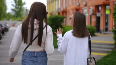 Şehir caddesinde kahve fincanı ile konuşan iki kendine güvenen genç kadının fotoğrafını çekiyorum. Arkadan bakıldığında zayıf beyaz kadın arkadaşları açık havada bulutlu bir sabahta geziniyorlar.