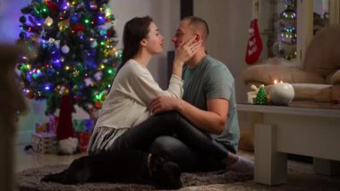 Odadaki Noel ağacında oturan genç ve pozitif bir çift. Yeni yıl ve Noel zamanı konsepti. Mutlu aile tatilleri