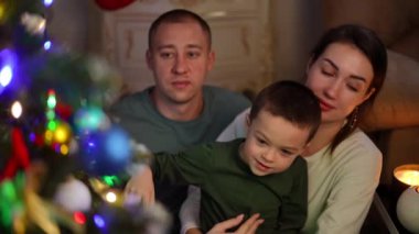 Ağır çekim. Baba, anne ve oğlunun Noel 'de Noel ağacının yanındaki evde boş vakitleri.