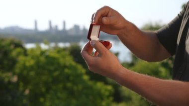 Bir adam, içinde yüzük olan kutuyu kapatır ve nehrin kenarındaki bir şehrin arka planına doğru elinde sıkar. Evlilik teklifi için hazırlanıyor.