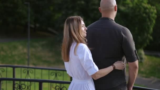一个女人从后面走近她心爱的男人 用胳膊轻轻拥抱着他 看着摄像机 春天公园里的浪漫时刻 — 图库视频影像