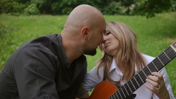 Ein Mann Küsst Seine Frau Die Gras Sitzt Und Gitarre — Stockvideo