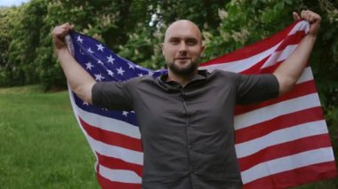 Amerikan bayrağı taşıyan bir adam şehir parkında Bağımsızlık Günü 'nü kutluyor.